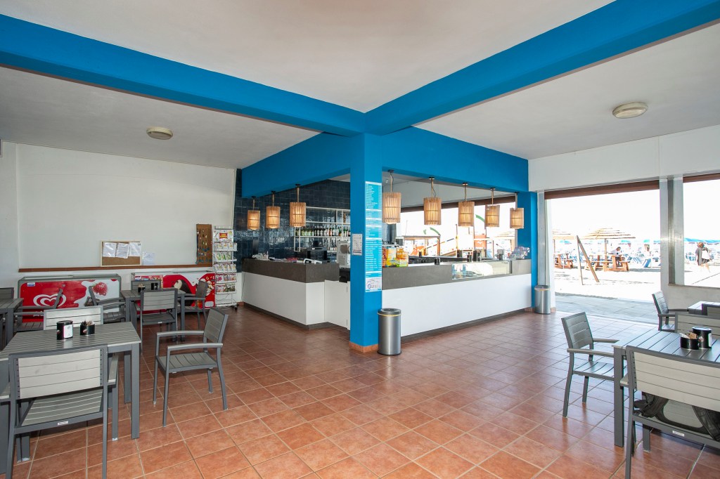 An empty beachside restaurant with a blue and white color scheme, featuring indoor seating areas and a counter-bar, with v...
