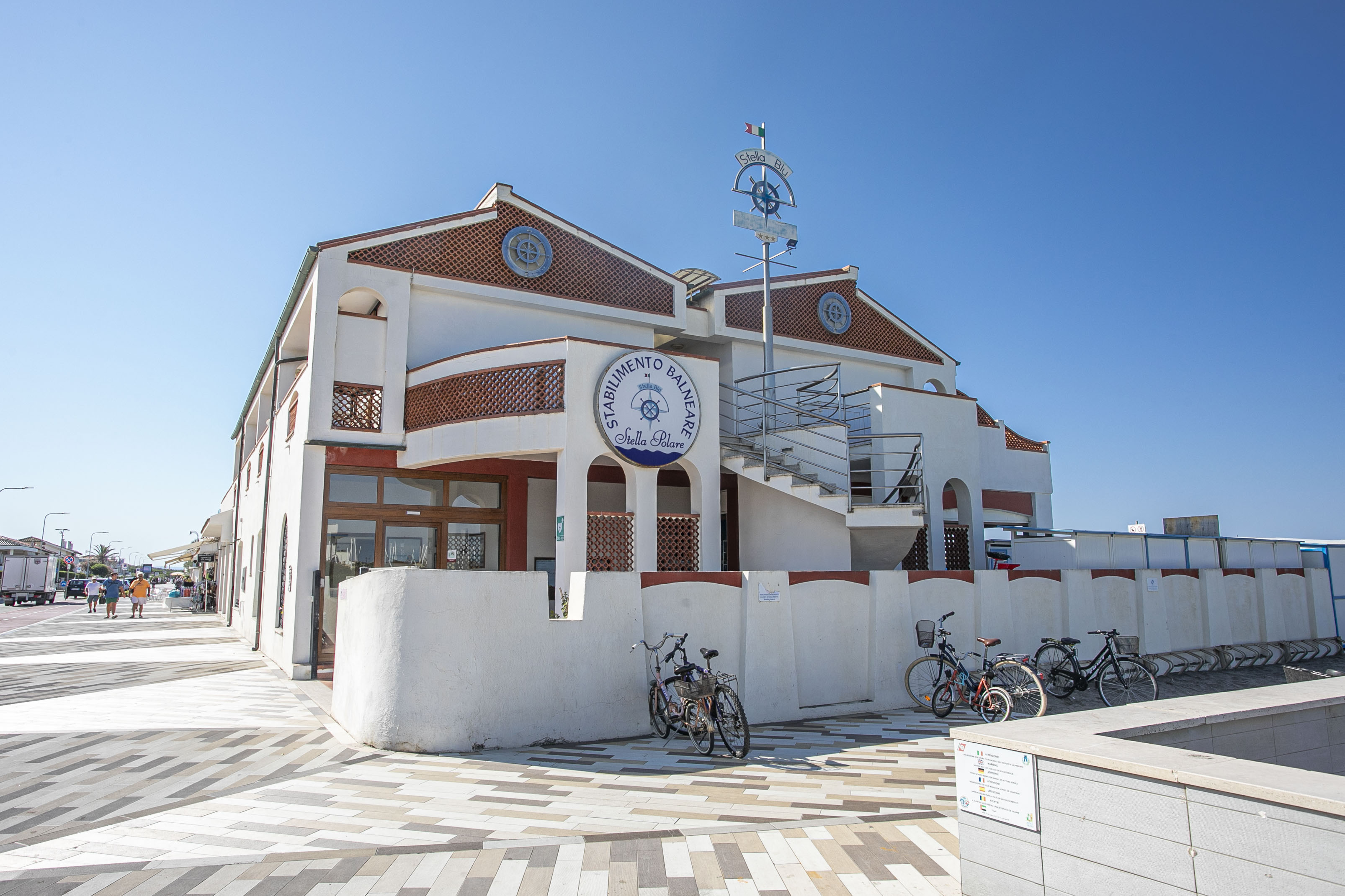 Building with signage, bicycles parked near, and pedestrians walking on street.