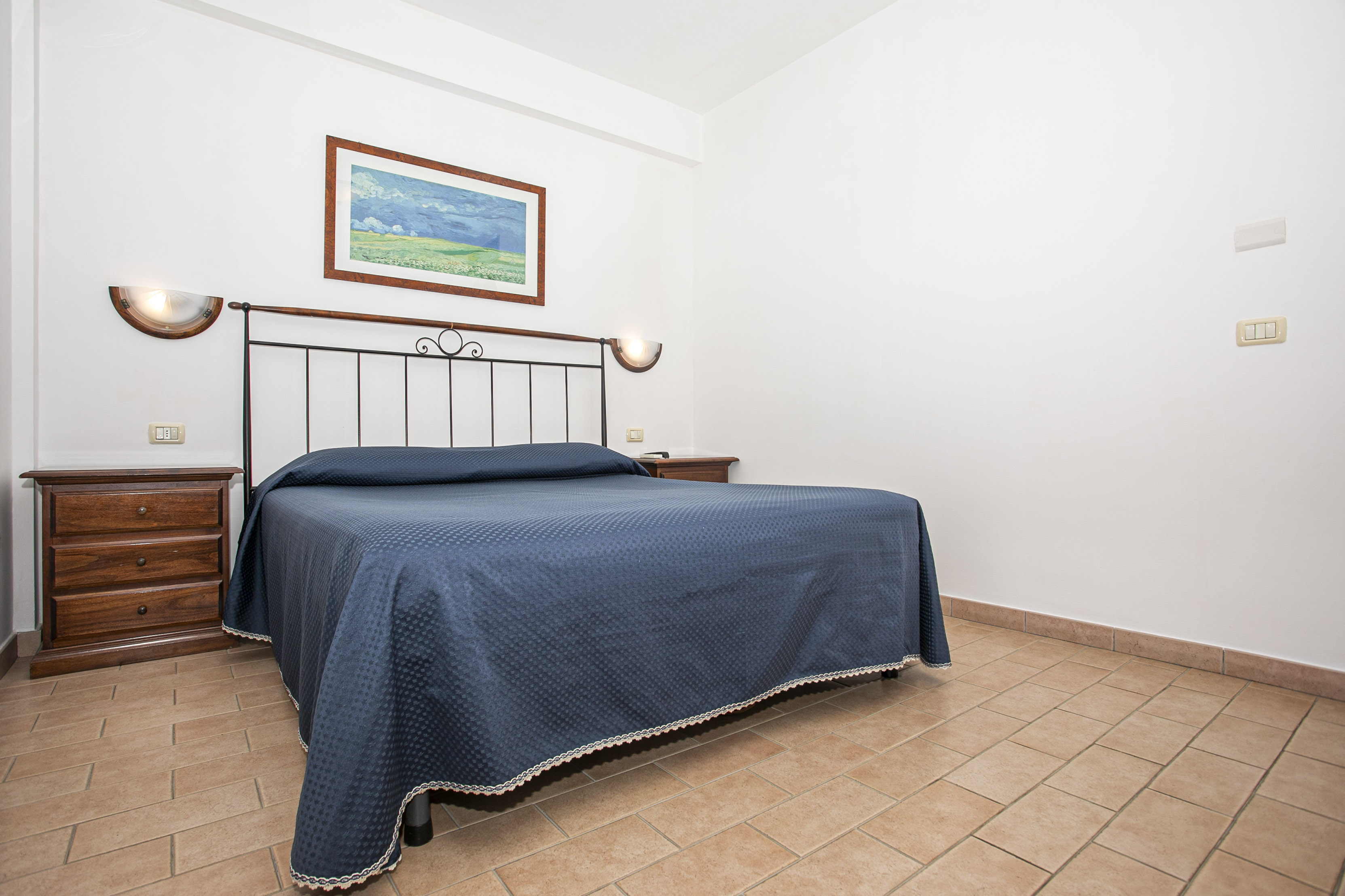 The image depicts a serene bedroom featuring a bed with a blue comforter and a white contrasting headboard, accompanied by...