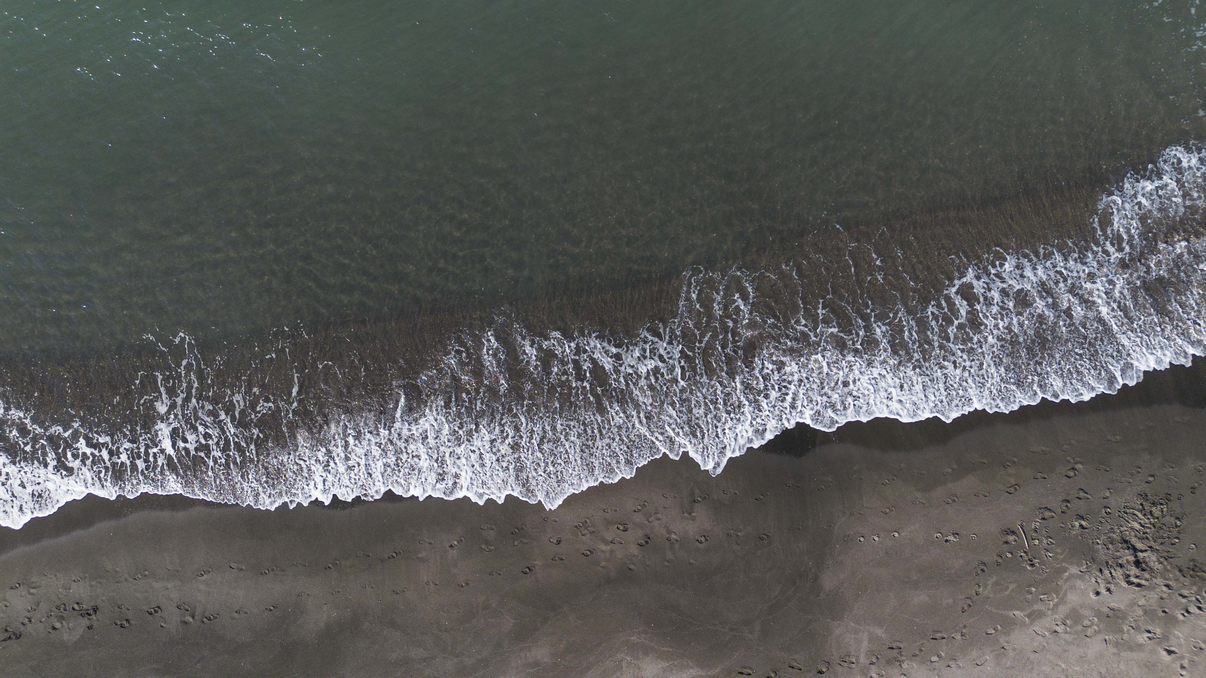 L'immagine mostra una scena naturale con il mare in primo piano, mentre una scia di onde bianche lancia ombre sugli scambi...